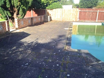 Swimming pool in a UK garden with clean slabs and a family enjoying a barbecue, showcasing swimming pool surround cleaning service